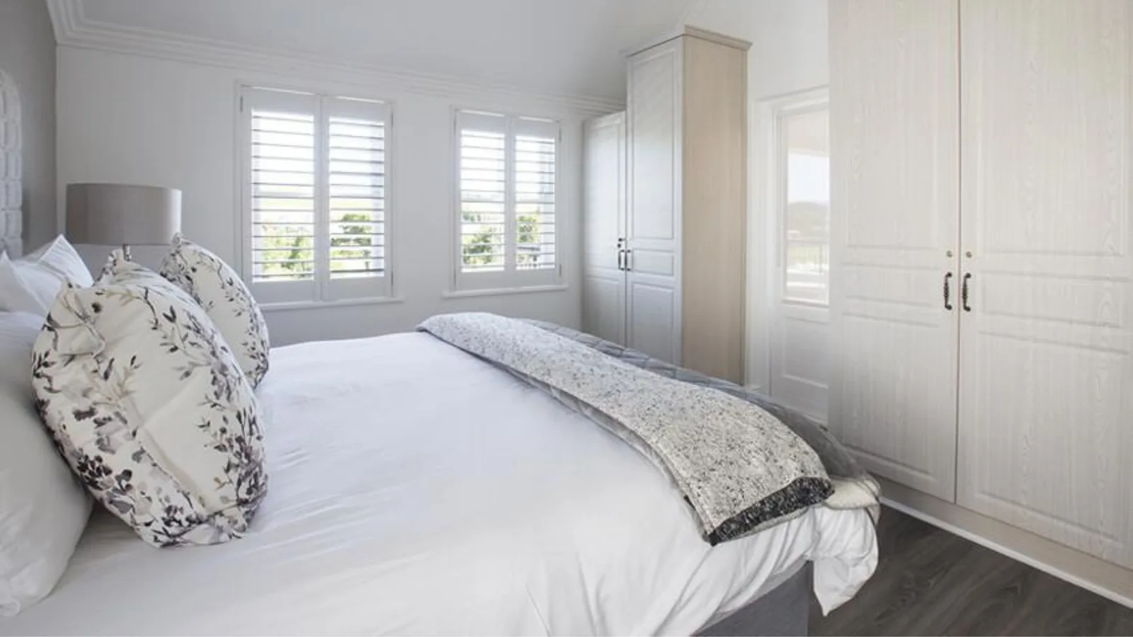 Elegantly styled double bedroom with floral cushions and plantation shutters at De Zalze