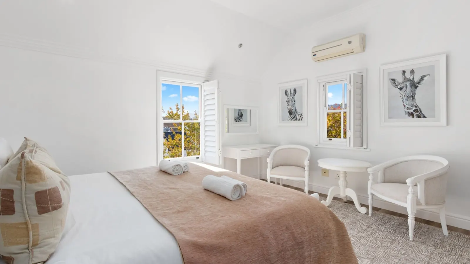 Bright white lodge bedroom with double bed, open shuttered windows and autumn foliage views at De Zalze Winelands Golf Lodges, Stellenbosch